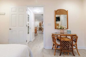 A hotel room with a bed, a dining area with wicker furniture, and a mirror on the wall. - Cypress Cove 103 - Beautiful 1 Bedroom 1 Bath Beachfront Condo in Biloxi (Biloxi)