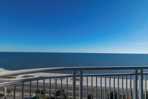 A coastal view from a balcony with a clear blue sky, a road with a roundabout, and the ocean in the background. - Beachview Condo at Legacy Tower 2 -1104 - Fully Furnished 2 Bedroom 2 Bath (Gulfport)