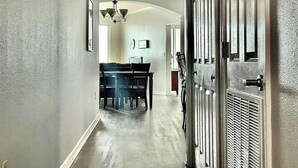 A hallway with a dining area, a chandelier, and a door with a vent. - Beachview Condo at Legacy Tower 2 -1104 - Fully Furnished 2 Bedroom 2 Bath (Gulfport)