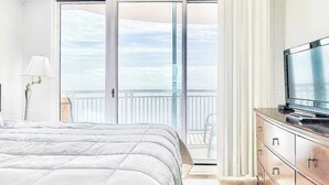 A bedroom with a large bed, a dresser, a television, and a balcony with a view of the sky. - Beachview Condo at Legacy Tower 2 -1104 - Fully Furnished 2 Bedroom 2 Bath (Gulfport)