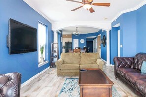 A living room with a TV, a ceiling fan, a sofa, a coffee table, and a patterned rug. - Spacious Beachview End Unit in Legacy Tower 2 -809 - 3 Bedroom 3 Bath Condo (Gulfport)