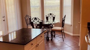 A kitchen with a central island, white cabinets, and a dining area with a table and chairs. - Legacy Villa 1306 - 2 Bedroom 2 Bath With Garage in Beachside Neighborhood (Gulfport)
