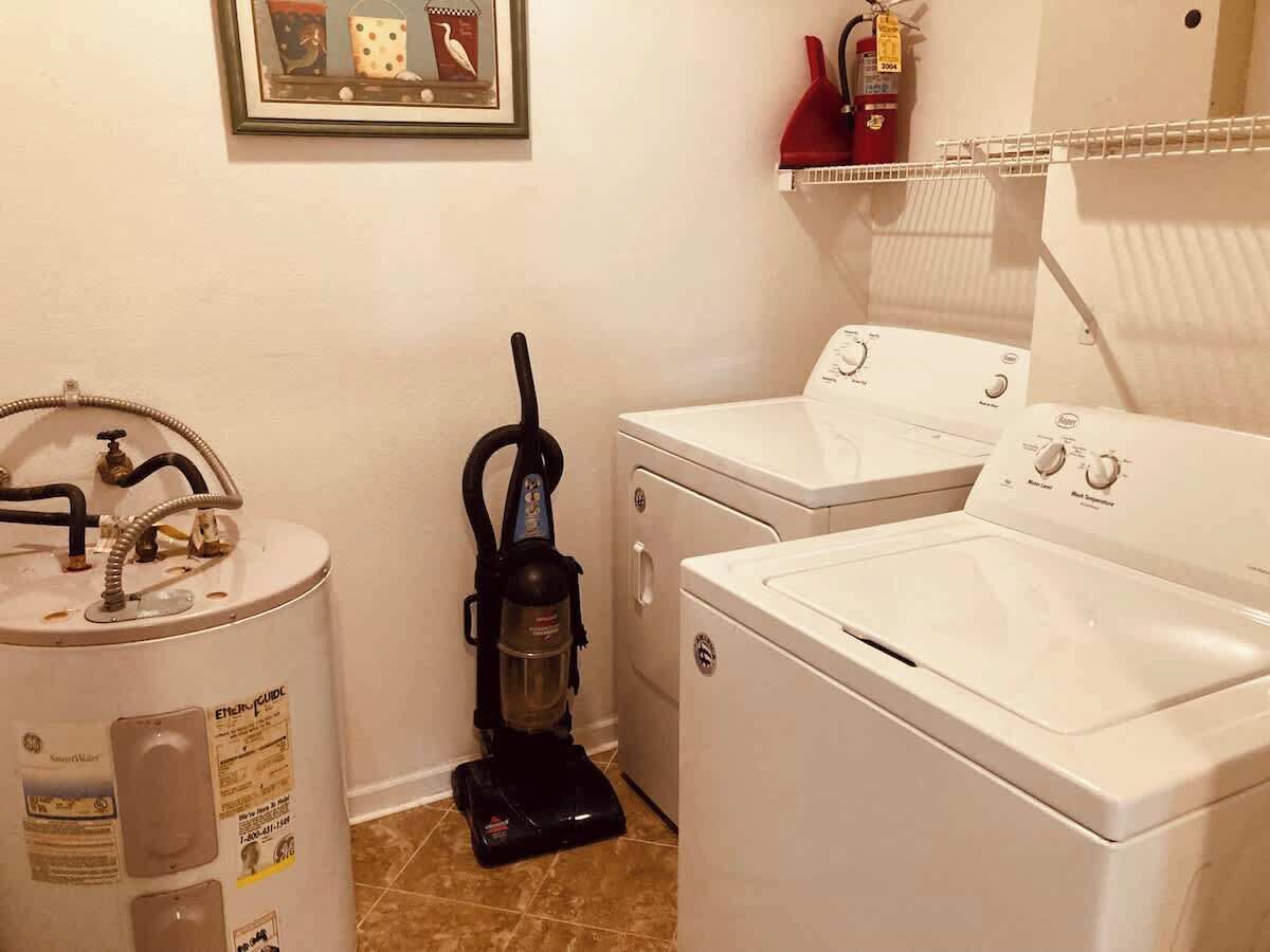 A laundry area with a water heater, a vacuum cleaner, and two washing machines.