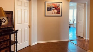 A hallway with white doors, a framed painting on the wall, and a dining area in the background. - Legacy Villa 1306 - 2 Bedroom 2 Bath With Garage in Beachside Neighborhood (Gulfport)