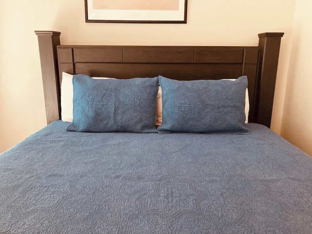 Una cama con cabecera oscura y dos almohadas.