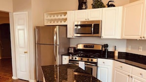 A modern kitchen with white cabinetry, stainless steel appliances, a granite countertop, and a black backsplash. - Legacy Villa 1306 - 2 Bedroom 2 Bath With Garage in Beachside Neighborhood (Gulfport)