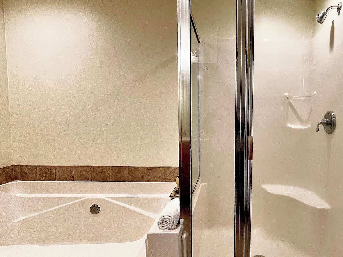 A glass-enclosed shower with a bathtub, a towel, and a glass container on the wall.