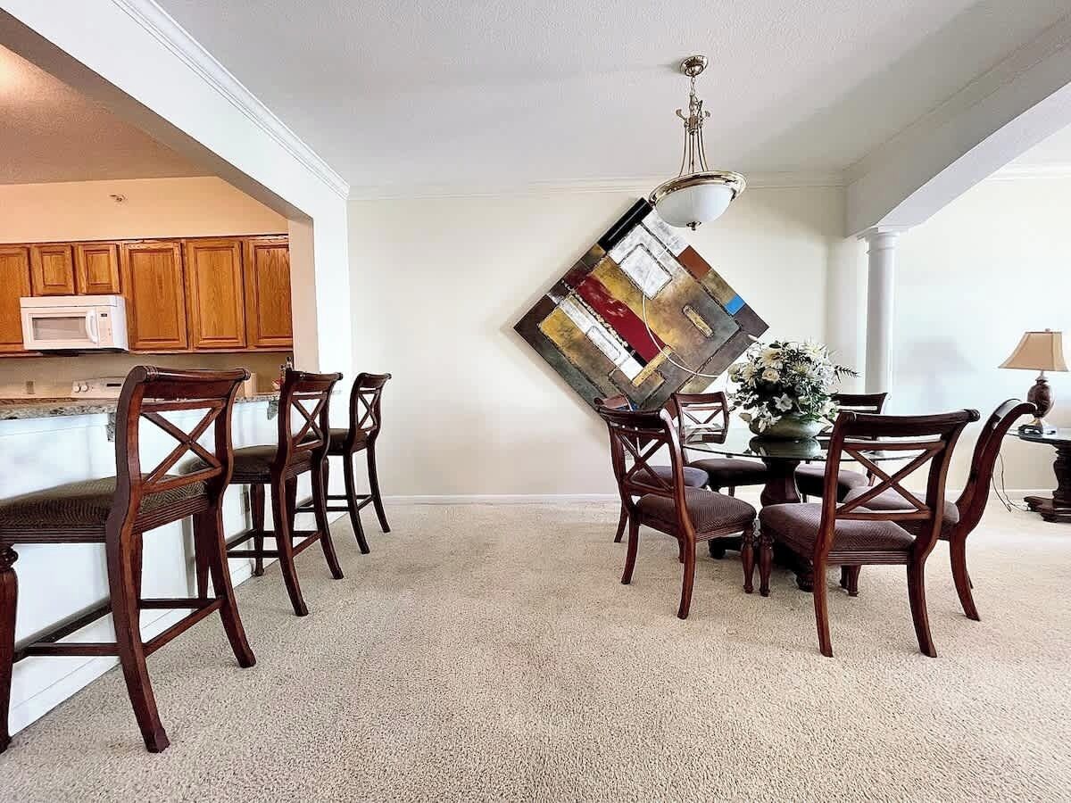 Un comedor con sillas y mesa de madera, una cocina con armarios de madera y un microondas, y una lámpara colgante.