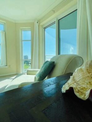 A room with a large window, a sofa, and a table. - Spacious Beachview End Unit in Legacy Tower 1 -1001 - 3 Bedroom 3 Bath Condo (Gulfport)