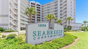 A sign for Seabreeze Condominiums with a clear view of the building's exterior, including multiple balconies and a well-maintained lawn.