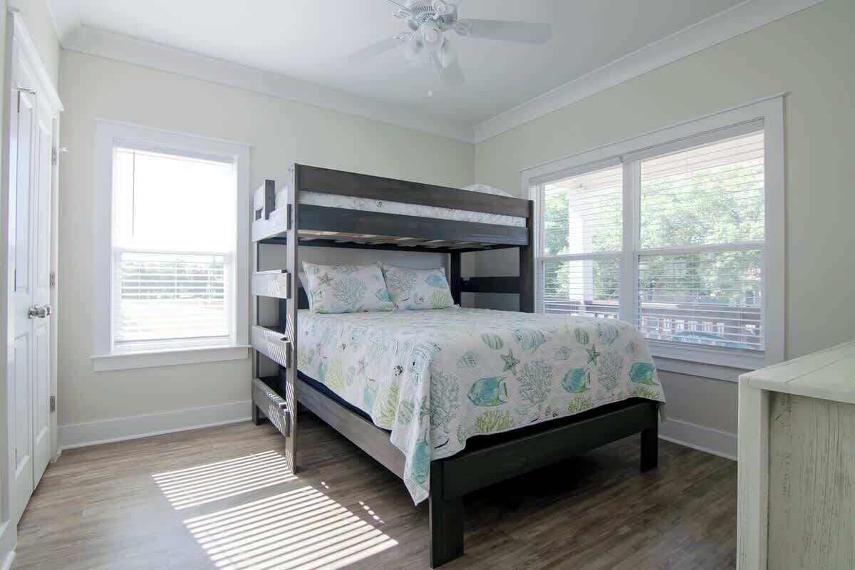 A bedroom with a bunk bed, a ceiling fan, and large windows.