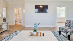Un salon spacieux doté d’un grand téléviseur à écran plat fixé au mur, d’une table basse agrémentée d’une plante en pot et d’un fauteuil à motifs.