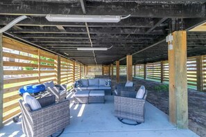 An outdoor covered patio with wicker furniture, a barbecue grill, and a concrete floor.
