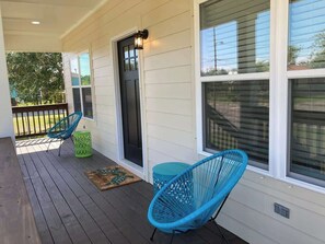 A covered porch with two blue chairs, a green stool, and a door with a black frame. - Brand New Home With Beach Views! Fully Furnished 3 Bedroom Home in Gulfport (Gulfport)