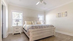 Une chambre à coucher avec un lit, des tables de chevet, un ventilateur de plafond et des fenêtres.