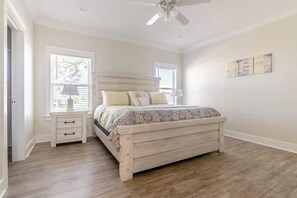 A bedroom with a bed, nightstands, a ceiling fan, and a window. - Brand New Home With Beach Views! Fully Furnished 3 Bedroom Home in Gulfport (Gulfport)