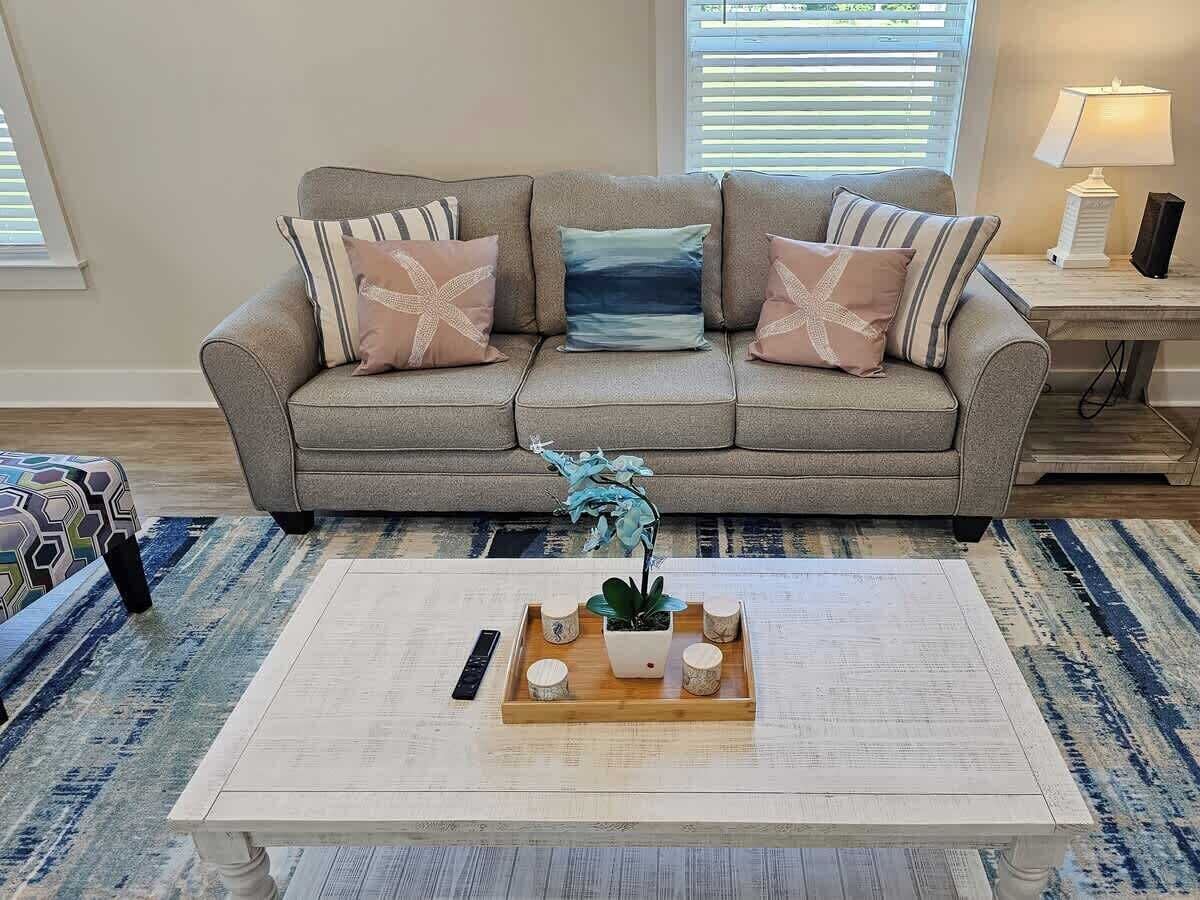 A living room with a grey sofa, patterned cushions, a coffee table with a tray of items, and a blue orchid plant.