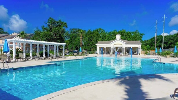 Ein Pool mit Liegestühlen und Sonnenschirmen, umgeben von Bäumen und einem Pavillon.