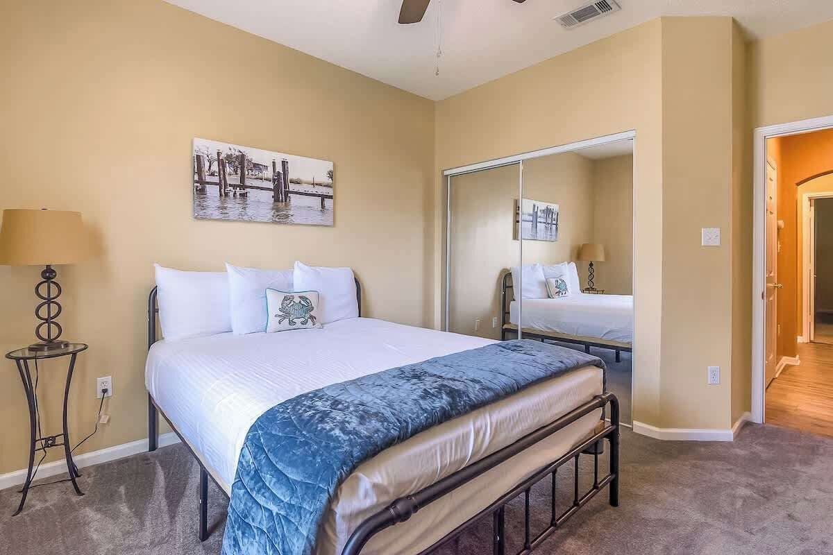 Een hotelkamer met een bed, een nachtkastje met een lamp, een grote spiegel en een schilderij aan de muur.