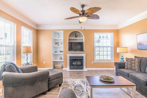 A living room with a fireplace, two sofas, a coffee table, and a ceiling fan. - Hideaway Shores (Gulfport)