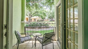 Ein Balkon mit zwei Stühlen und einem kleinen Tisch, mit Blick auf eine grüne Rasenfläche und eine Straße.