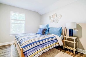 A bedroom with a bed, a nightstand, a lamp, and wall decorations. - Brand New, Fully Furnished 3 Bedroom, 3 Bathroom Home in Ocean Springs! (Ocean Springs)