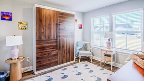 A modern room with a large wardrobe, a small table with a lamp, a chair, and a window with blinds. - Brand New, Fully Furnished 3 Bedroom, 3 Bathroom Home in Ocean Springs! (Ocean Springs)