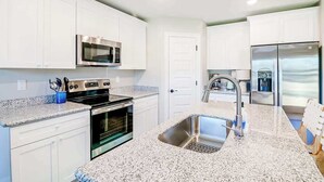 A modern kitchen with white cabinets, stainless steel appliances, granite countertops, and a double sink. - Brand New, Fully Furnished 3 Bedroom, 3 Bathroom Home in Ocean Springs! (Ocean Springs)