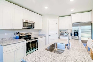 A modern kitchen with white cabinets, stainless steel appliances, granite countertops, and a double sink. - Brand New, Fully Furnished 3 Bedroom, 3 Bathroom Home in Ocean Springs! (Ocean Springs)