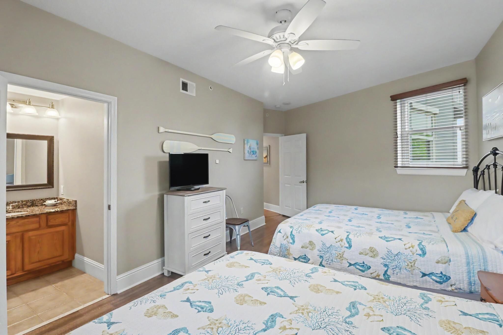 A bedroom with two beds, a television, a ceiling fan, and a bathroom with a vanity and mirror.