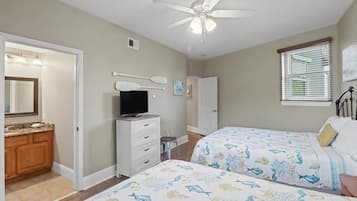 A bedroom with two beds, a television, a ceiling fan, and a bathroom with a vanity and mirror.