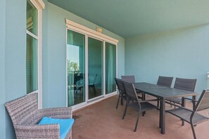 Un patio cubierto con una mesa y sillas, un sofá de mimbre y un ventanal corredizo que da a un espacio al aire libre.
