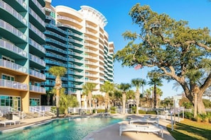 A hotel with a large pool area, outdoor seating, and a prominent American flag. - Quiet Beachview End Unit in Legacy Tower 2 -309 - 3 Bedroom 3 Bath Condo (Gulfport)