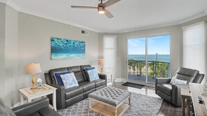 A modern living room with a black leather sofa, a grey tufted ottoman, and a ceiling fan. - Shoreline Retreat (Gulfport)