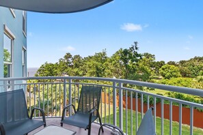 Un balcón con una mesa y sillas, con vista a un jardín con árboles y una valla.