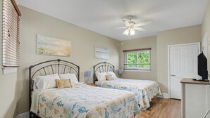 A bedroom with two beds, a ceiling fan, and artwork on the walls. - Shoreline Retreat (Gulfport)