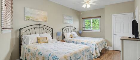 A bedroom with two beds, a ceiling fan, and artwork on the walls.
