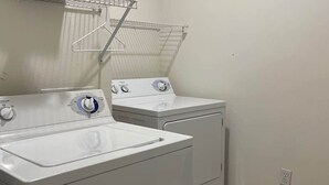 Une buanderie équipée de deux machines à laver et deux sèche-linge superposés, d’un étendoir métallique et d’une prise de courant au mur.