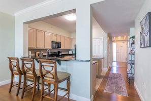 A kitchen with wooden cabinets, a central island with bar stools, and a hallway leading to a door.