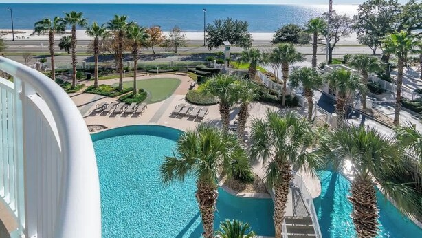 A pool area with palm trees, a view of the beach, and a clear sky.