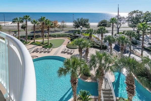 A pool area with palm trees, a view of the beach, and a clear sky.