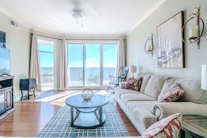A living room with a sofa, a coffee table, a TV, and a balcony with a view.