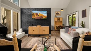 A modern living room with a black brick accent wall, a large painting, a dining area, and a cozy seating arrangement. - Lush Backyard, Hot Tub, Grill, Covered Patio (Sedona)