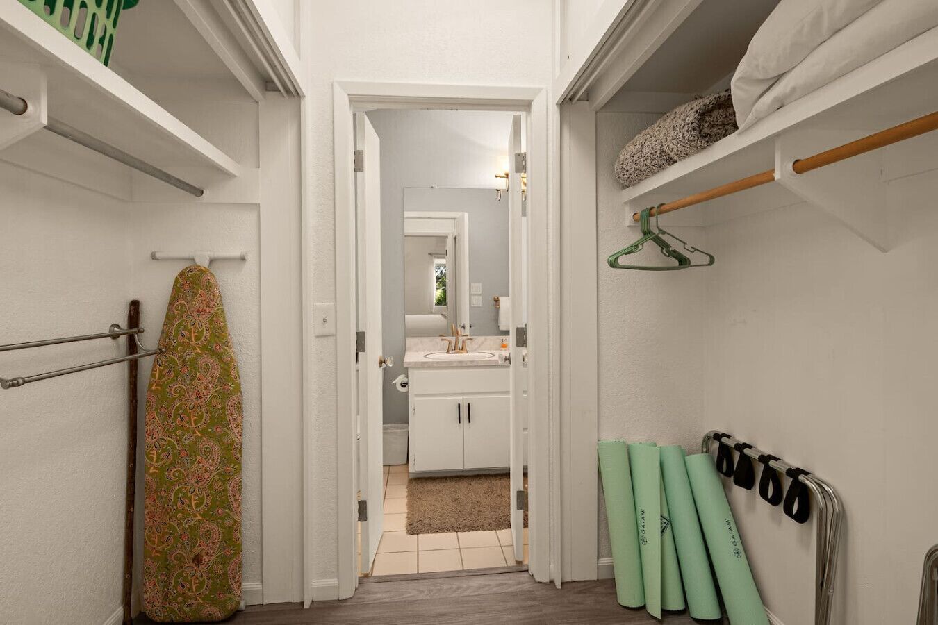 Un pasillo estrecho que conduce a un baño con espejo, lavamanos y toallero.