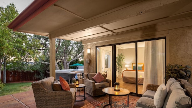 A covered patio area with wicker furniture, a hot tub, and a view of a bedroom with a bed and nightstand. - Lush Backyard, Hot Tub, Grill, Covered Patio (Sedona)