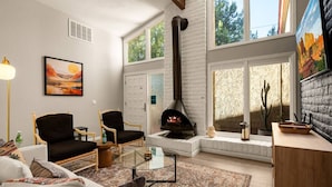 A cozy living room with a fireplace, comfortable seating, and large windows offering views of the outdoors. - Lush Backyard, Hot Tub, Grill, Covered Patio (Sedona)
