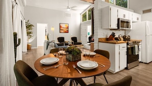 A modern kitchen with white cabinets, a built-in oven, and a microwave. There is a dining area with a wooden table set for two, and a cozy seating area with a fireplace. - Lush Backyard, Hot Tub, Grill, Covered Patio (Sedona)