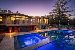 A pool with a stone border, a deck with lounge chairs, and a building with a balcony.