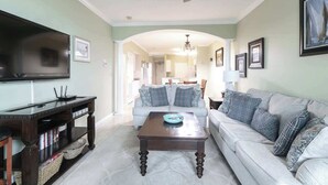 A living room with a flat-screen TV, a wooden coffee table, a sofa, and a bookshelf. - Beachview Condo in Legacy Tower1 -303 - With Reserved Parking Spot in Front (Gulfport)
