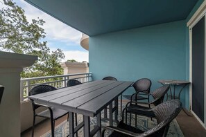 Un balcon avec une table et des chaises, une petite table ronde et une vue sur les arbres et les bâtiments.